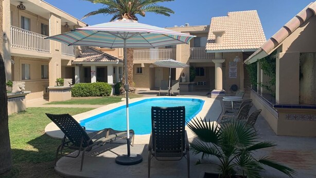 A pool area with lounge chairs and umbrellas, surrounded by a building with a tiled roof and a palm tree. - Hotel Maripina (Ciudad Juárez)