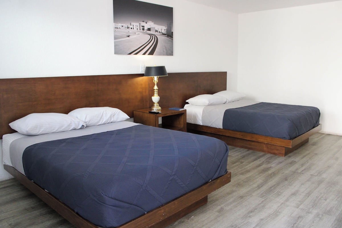 A hotel room with two beds, a nightstand with a lamp, and a wall-mounted picture.
