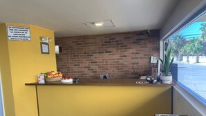 A reception area with a yellow counter, a brick wall, and a window with a view of palm trees. - Hotel Maripina (Ciudad Juárez)