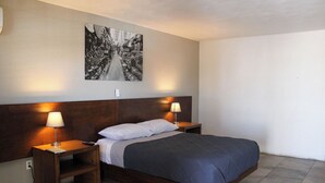 A neatly arranged bedroom with a wooden headboard, a single bed with a dark blue bedspread, two bedside lamps, and a black and white photograph on the wall. - Hotel Maripina (Ciudad Juárez)