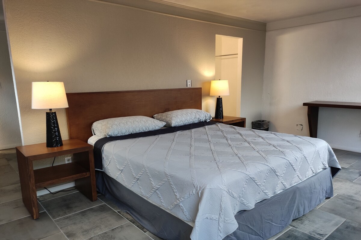 A neatly made bed with a quilted cover, two bedside lamps, and a wooden nightstand.