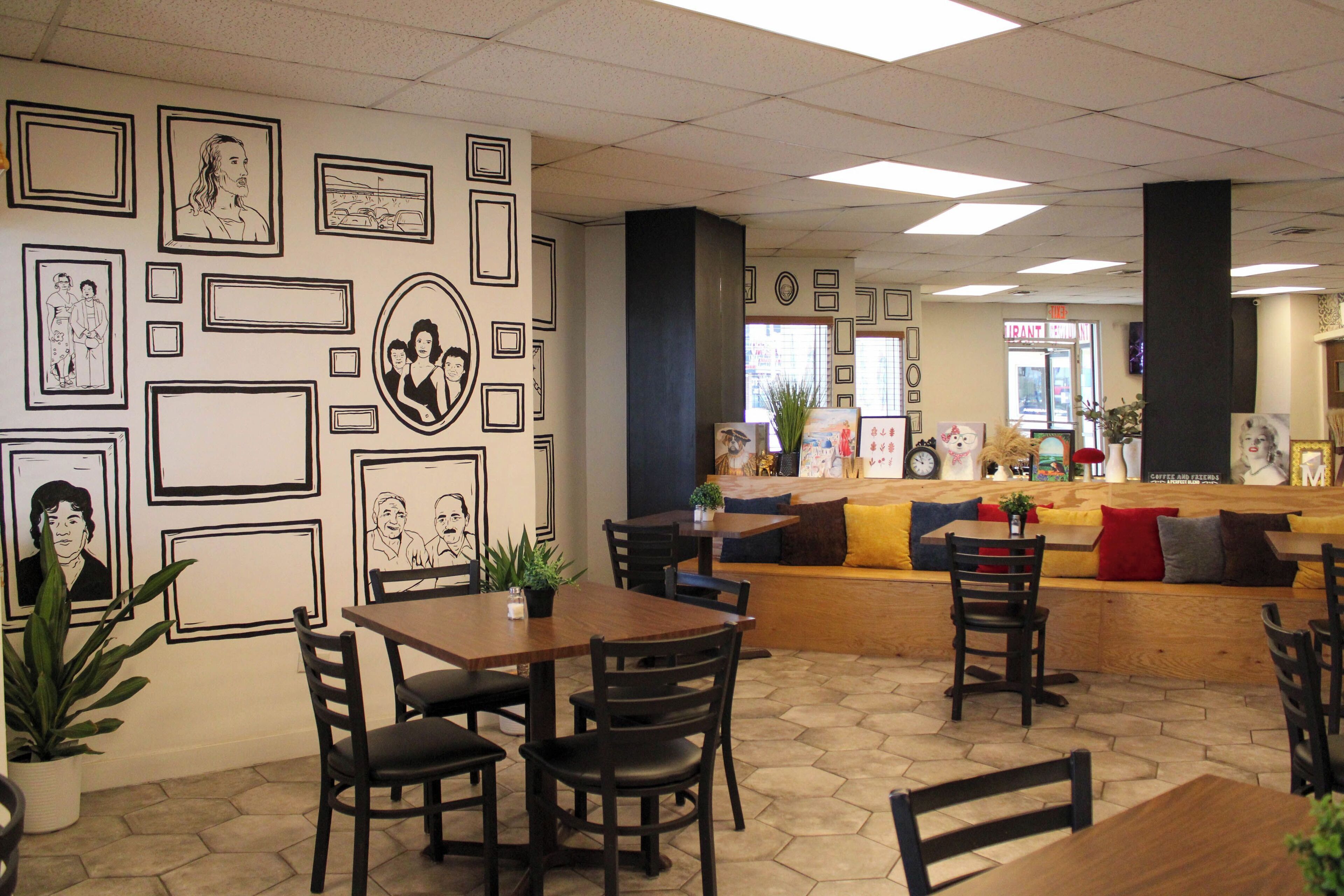 A cafe with wooden tables and chairs, a counter with a menu, and a wall decorated with framed pictures.