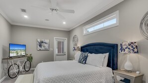 A bedroom with a large bed, a ceiling fan, a television, and a bicycle. - Modern Beach Retreat • Hot Tub • Private Beach Access • Sleeps 10 (Miramar Beach)
