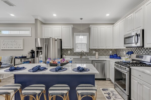 A modern kitchen with white cabinets, stainless steel appliances, a central island with stools, and a backsplash with a geometric pattern.