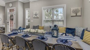 A dining area with a long table, chairs, and a bench. There are decorative pillows and a lantern on the bench. - Modern Beach Retreat • Hot Tub • Private Beach Access • Sleeps 10 (Miramar Beach)