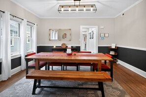 A dining room with a wooden table, red chairs, a chandelier, and a view of the outside through large windows. - Fully Fenced, Dogs Welcome, Sleeps 10, Near MSU and Hospitals (Springfield)