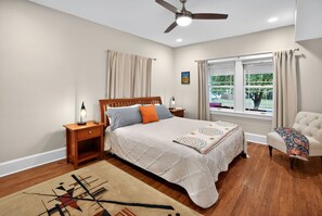 A bedroom with a bed, nightstands, a ceiling fan, a window with curtains, and a chair. - Fully Fenced, Dogs Welcome, Sleeps 10, Near MSU and Hospitals (Springfield)
