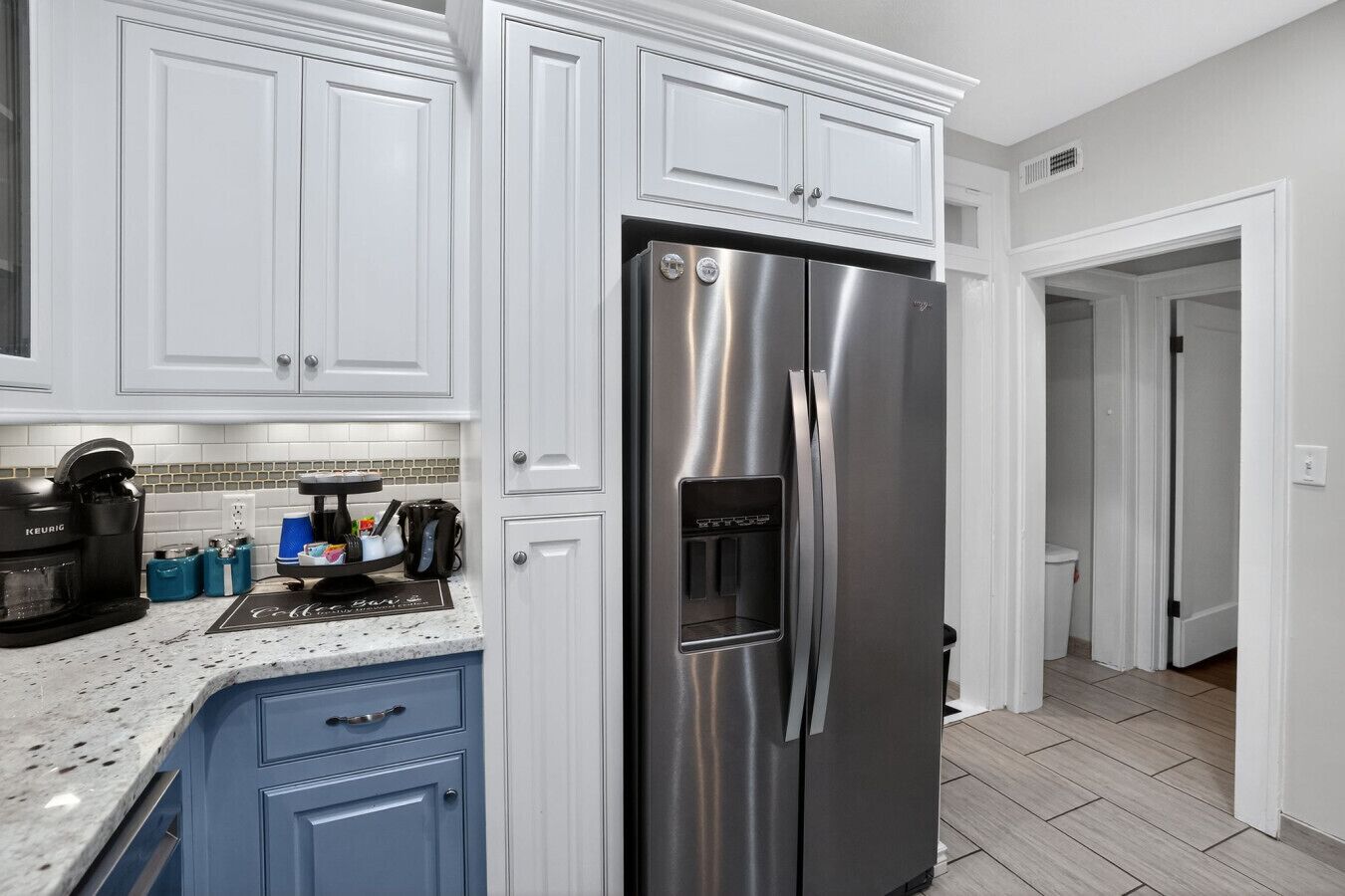 A modern kitchen with white cabinetry, a stainless steel refrigerator, a coffee maker, and a built-in water dispenser.