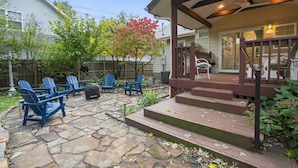 A patio area with stone flooring, blue Adirondack chairs, a covered porch, and a wooden staircase leading to a deck. - Fully Fenced, Dogs Welcome, Sleeps 10, Near MSU and Hospitals (Springfield)
