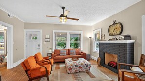 A living room with a fireplace, a ceiling fan, and a clock on the wall. - Fully Fenced, Dogs Welcome, Sleeps 10, Near MSU and Hospitals (Springfield)