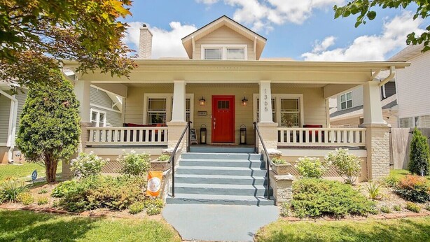 A two-story house with a red front door, a covered porch with steps, and a stone chimney. - Fully Fenced, Dogs Welcome, Sleeps 10, Near MSU and Hospitals (Springfield)