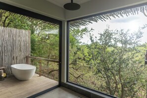 Une salle de bain moderne avec une grande baignoire, une terrasse en bois et une vue sur une zone boisée.