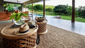 A modern living room with a large glass window, a pool, and a view of a lush garden. - Sungulwane Private Game Lodge (Hluhluwe)