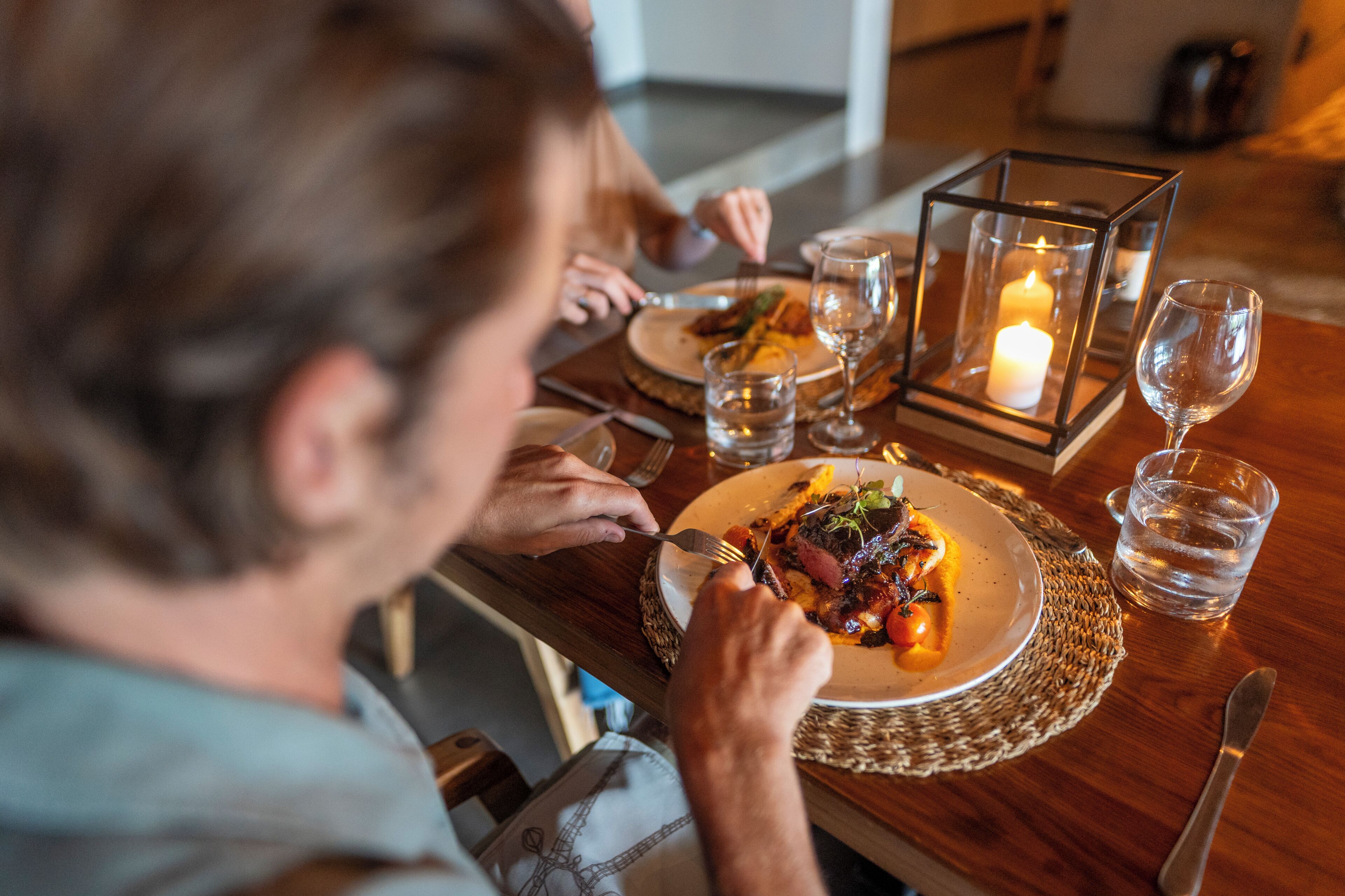A dining table with a candle, glasses, and a plate of food.