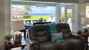 A living room with a leather sofa, a dining table set, and a view of the ocean through large glass doors. - Lux 3 Bdrm Ocean Front villa with Private pool! (Lowlands)