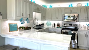 A kitchen with white cabinets, a central island, stainless steel appliances, and teal kitchen towels. - Lux 3 Bdrm Ocean Front villa with Private pool! (Lowlands)