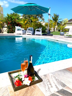 A poolside area with lounge chairs, a table with a bottle of champagne and glasses, and a tray with flowers. - Lux 3 Bdrm Ocean Front villa with Private pool! (Lowlands)