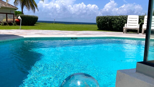 A clear blue pool with a glass ball containing seashells, surrounded by lounge chairs and palm trees. - Lux 3 Bdrm Ocean Front villa with Private pool! (Lowlands)