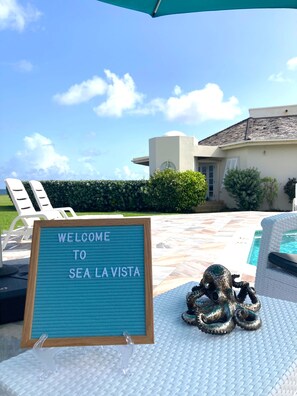 A sign reading "WELCOME TO SEA LA VISTA" by a pool with lounge chairs and a decorative octopus sculpture. - Lux 3 Bdrm Ocean Front villa with Private pool! (Lowlands)
