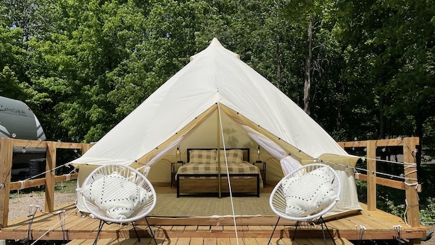 A tented accommodation with a bed, two white hanging chairs, and a patterned rug on a wooden deck. - Beautiful experience on Gull Lake. (Nisswa)