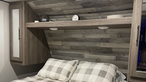 A bedroom with a checkered bedspread, wooden headboard, and built-in shelving with a clock and decorative items. - Beautiful experience on Gull Lake. (Nisswa)