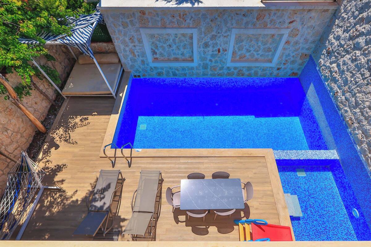 Uma piscina ao ar livre com um deque de madeira, espreguiçadeiras e uma mesa.
