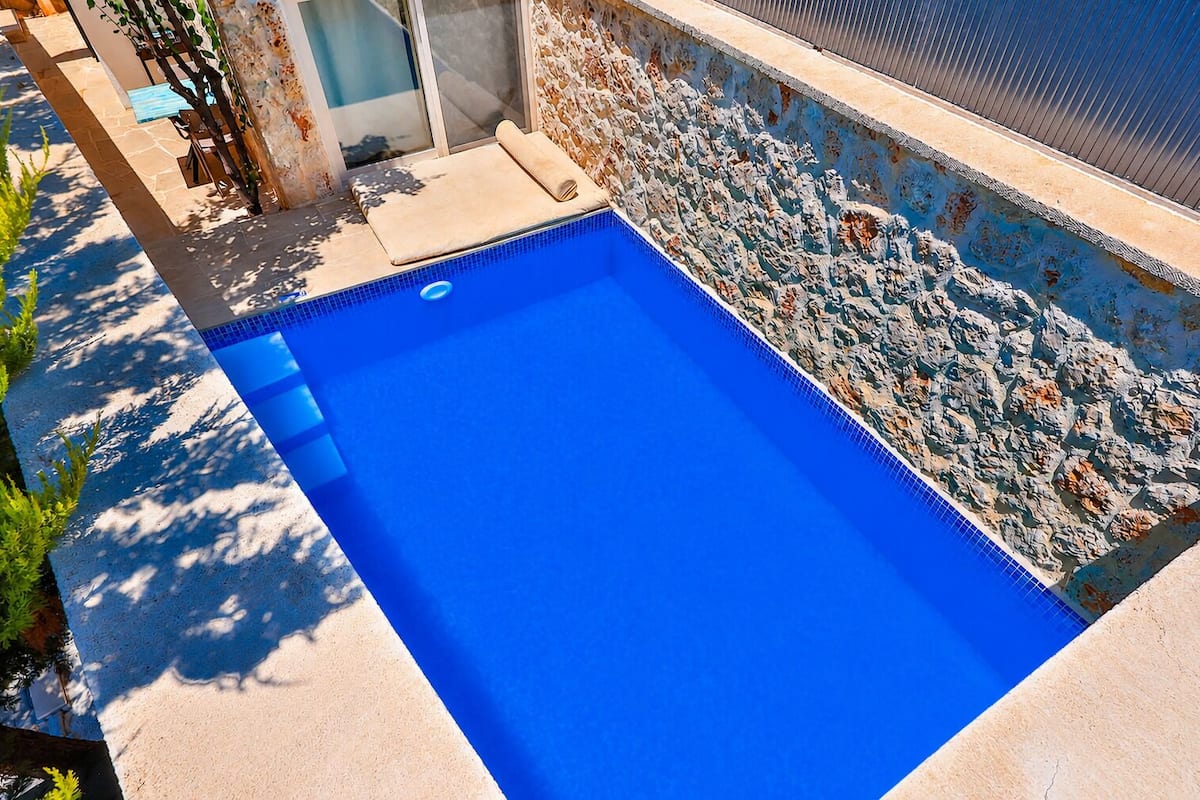 Piscina retangular com interior azul, rodeada por uma parede de pedra e um deck revestido com azulejos.