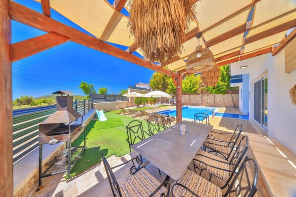 Une terrasse extérieure avec un barbecue, un espace salon et une piscine.
