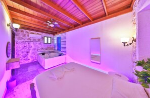 Une pièce avec un mur en pierre, des poutres en bois au plafond, une baignoire, un lit et un miroir.
