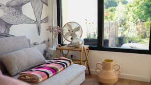 A cozy room with a sofa, a woven chair, a large window with a view of greenery, and a wooden vase. - Les Hirondelles, beautiful house with garden for 7 people (Saint-Valery-sur-Somme)