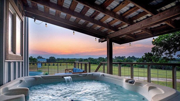Ein Whirlpool unter einer Holzpergola mit Blick auf eine Rasenfläche und Bäume.
