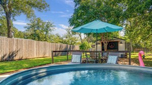 Un giardino sul retro con piscina, recinzione in legno, patio con sedie e tavolo, e una decorazione a forma di fenicottero.