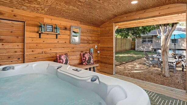 Interno di una baita in legno con vasca idromassaggio, pareti in legno, una panca con cuscini e vista sul giardino.