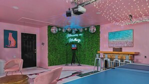 Una stanza con tavolo da ping pong, insegna luminosa, palle da discoteca e parete verde.