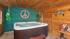 Interno di una baita in legno con vasca idromassaggio, un simbolo della pace e un cartello con scritto 'Good Vibes Only'.
