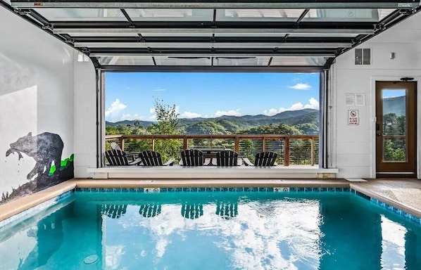 Ein Schwimmbecken mit Bergblick, eine Holzterrasse mit Stühlen und ein Wandgemälde an der Wand.