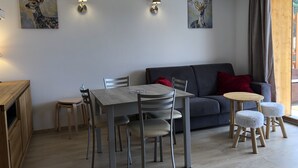 A dining area with a table and chairs, a sofa, and artwork on the walls. - Charming T3 in a residence close to the slopes and shops South-facing balcony (La joue du loup)