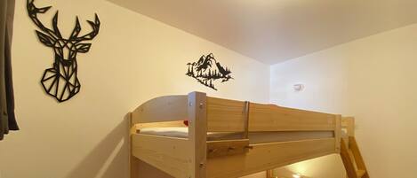 A bunk bed with a red mattress and a pillow, a wall decal of a deer, and a mountain scene.