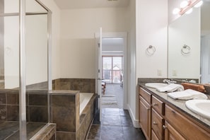 Un baño moderno con cabina de ducha de vidrio, bañera, tocador con un espejo grande y vistas al exterior.