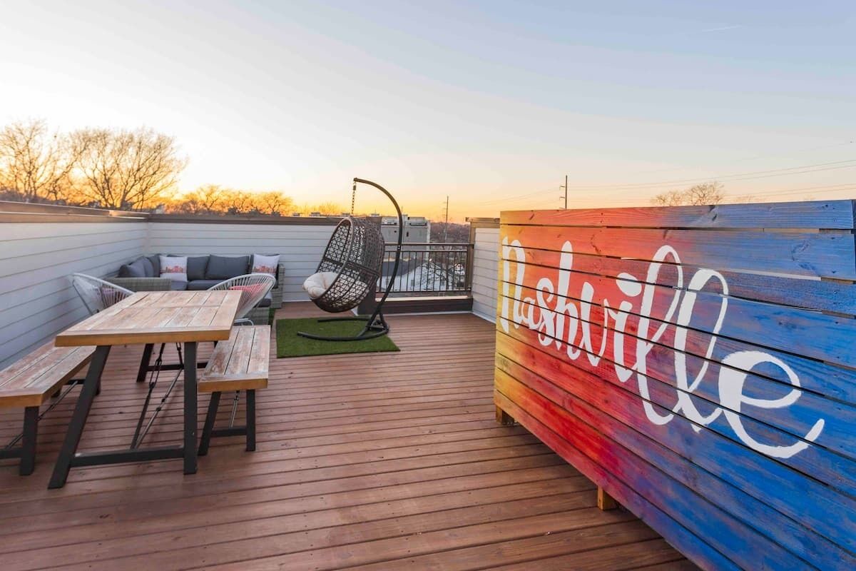 A wooden deck with a picnic table, a cushioned seating area, and a colorful wall with the word "Lighthouse".