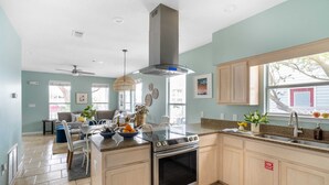 Une cuisine dotée d’un grand îlot central, d’appareils électroménagers en acier inoxydable et d’une fenêtre donnant sur une maison.