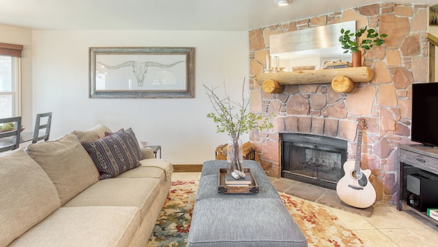 A living room with a stone fireplace, a sofa, a coffee table, and a guitar. - Snow King by Avantstay Close to the Slopes w/ Hot Tub! (Park City)