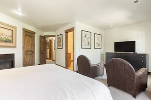 A bedroom with a large bed, a TV, a fireplace, and framed pictures on the wall.