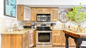 A kitchen with wooden cabinets, a stainless steel oven, a microwave, and a decorative wall clock. - Snow King by Avantstay Close to the Slopes w/ Hot Tub! (Park City)