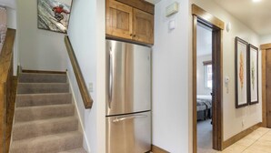 A kitchen with a stainless steel refrigerator, wooden cabinets, and a staircase leading to another room. - Snow King by Avantstay Close to the Slopes w/ Hot Tub! (Park City)
