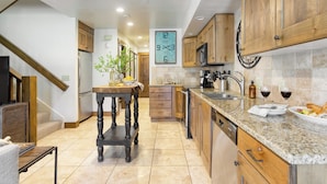 A kitchen with wooden cabinets, a granite countertop, a clock, and a dining area with a table and chairs. - Snow King by Avantstay Close to the Slopes w/ Hot Tub! (Park City)