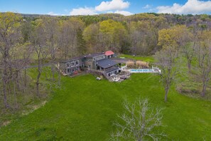 Une grande maison avec une piscine, entourée d’une pelouse verdoyante et d’arbres.