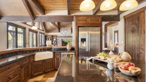 A spacious kitchen with dark wooden cabinets, a large island with a sink, and a stainless steel refrigerator. - Big Pine by Avantstay Stunning Secluded Oregon Home w/ Hot Tub (Bend)