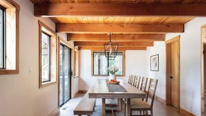 A spacious dining area with a wooden table and benches, large windows, and a hanging light fixture. - Timberline by Avantstay Stunning Chalet Cabin w/ Hot Tub, Pool Table & Home Theater! (Carnelian Bay)