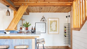 Une cuisine avec un plafond en bois, un coin bar avec des tabourets, un meuble à vin et des œuvres d’art encadrées accrochées au mur.